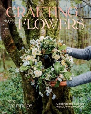 Book cover for Crafting with Flowers by Bex Partridge featuring a floral wreath held up against a tree. The wreath is made from spring flowers such as daffodils, primroses and spring greenery.