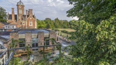 Aerial view looking east over the Flood Resilient Garden to the manor house. Galvanised steel pergola, recycled stone paving, recycled wooden deck benches and tables, galvanised water tank features and pond. The Flood Resilient Garden at Howbery Park