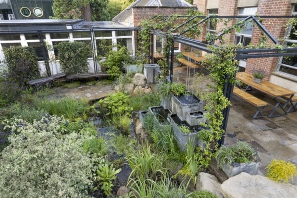 Aerial view over the Flood Resilient Garden. Galvanised steel pergola with climbing plants, recycled stone paving, recycled wooden deck benches and tables, galvanised water tank features and pond.The Flood Resilient Garden at Howbery Park