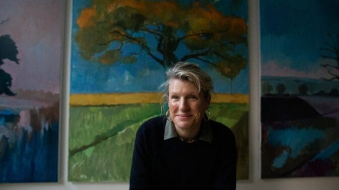 Image of the artist Nancy Cadogan,in front of her paintings of trees